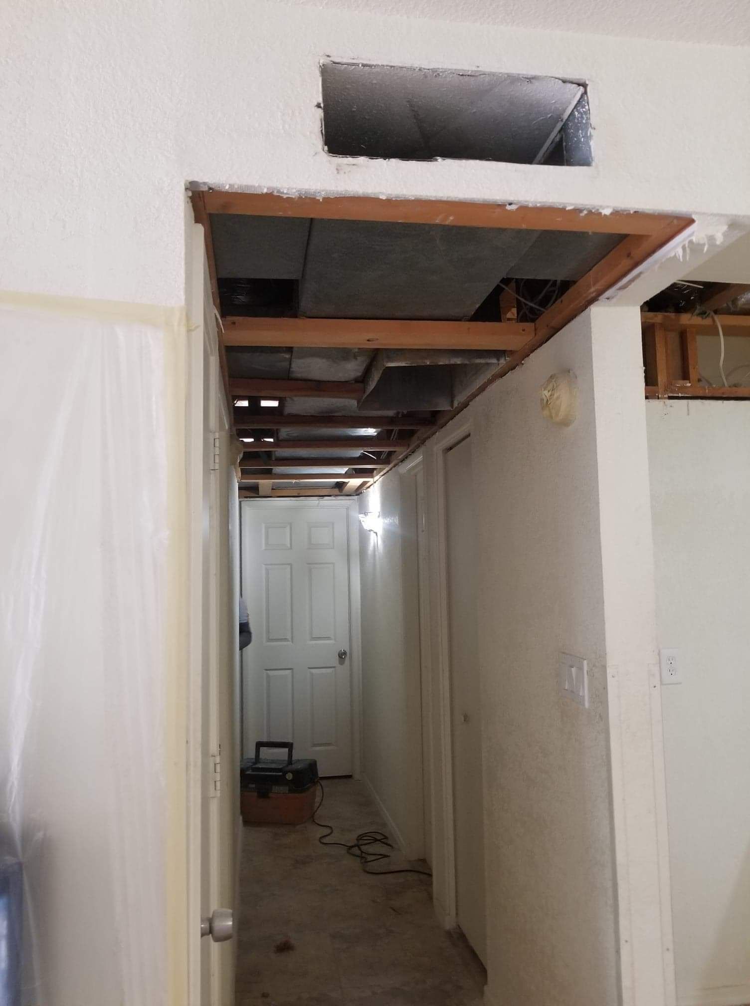 Narrow hallway under construction with exposed ceiling, white walls, and a door at the end