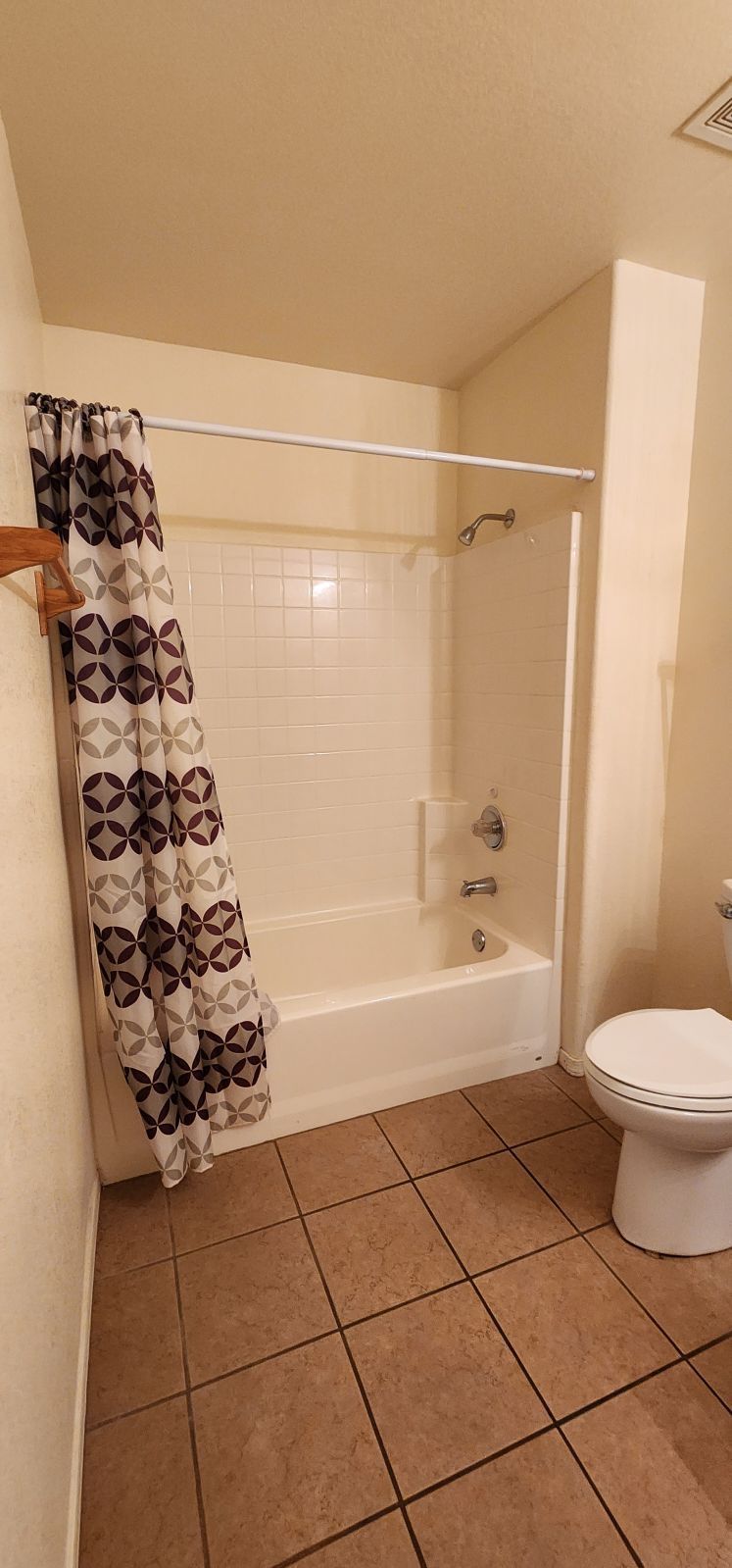 Small beige bathroom with a white bathtub, patterned shower curtain, and toilet beside tiled floor.