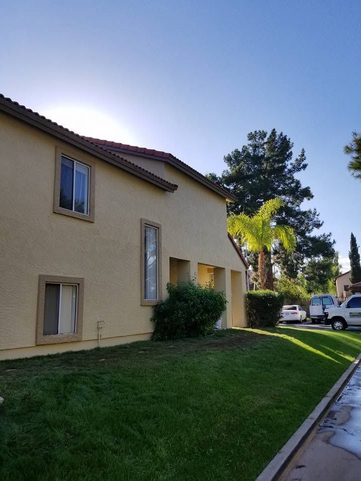Residential building with beige stucco walls, green lawn, and parked cars on a sunny day