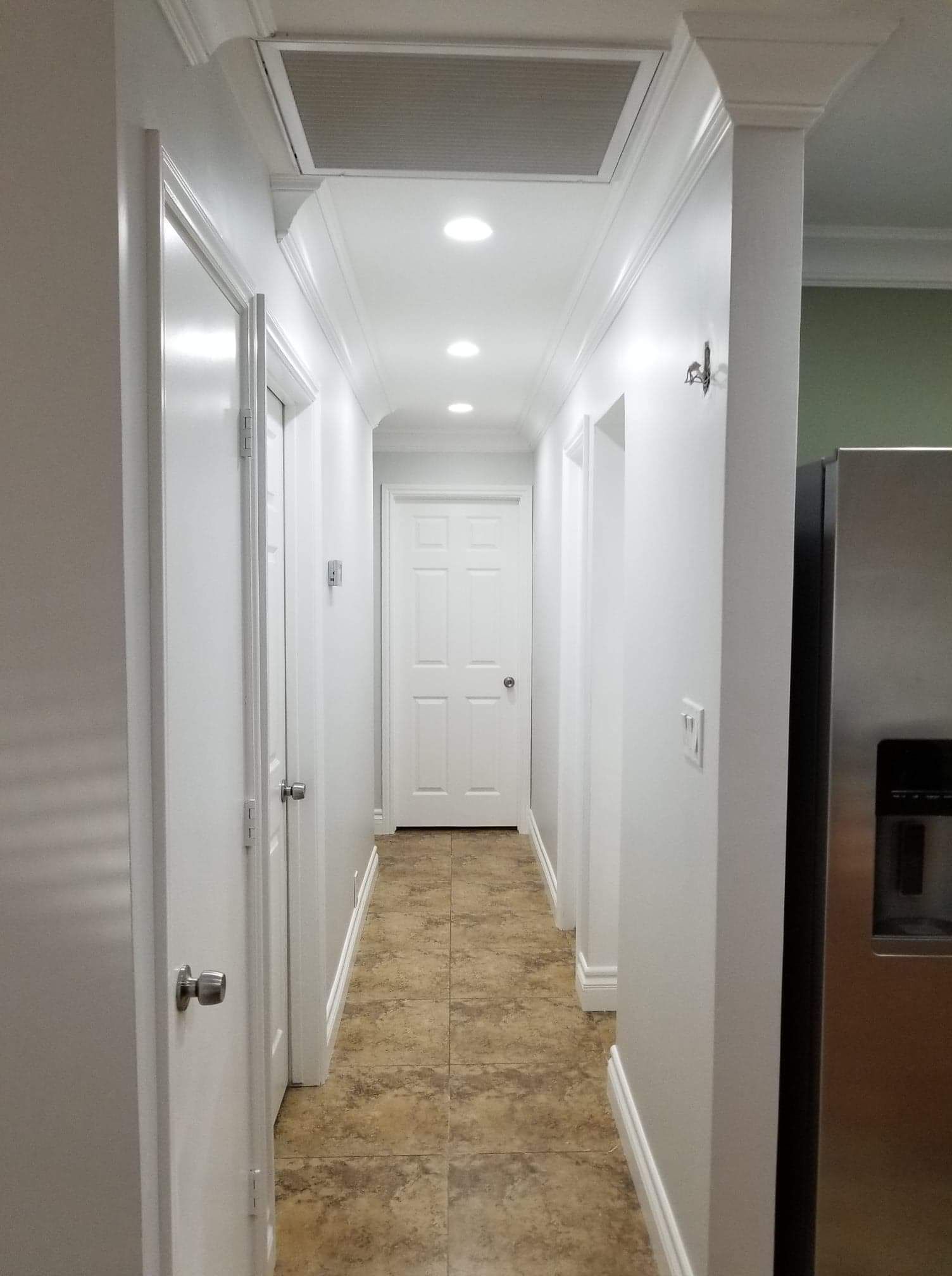 Long white hallway with recessed lights, beige tile floor, and closed doors at the end