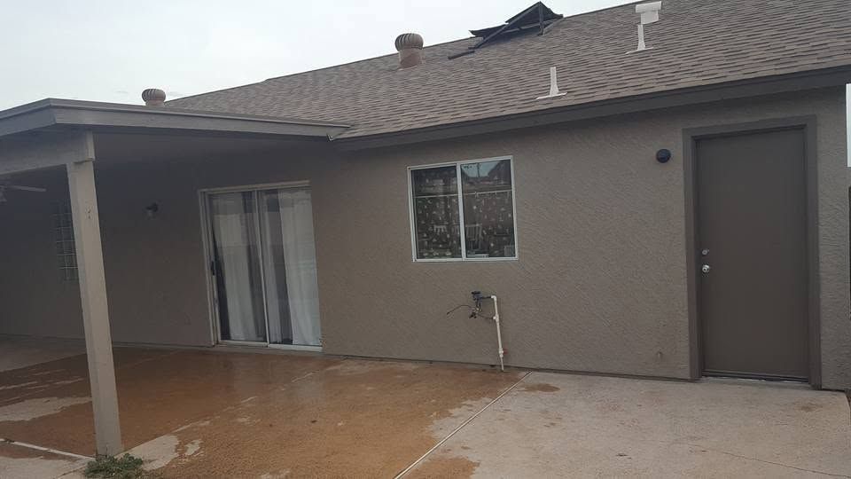 Backyard view of a beige house with sliding glass door, small window, and covered patio area