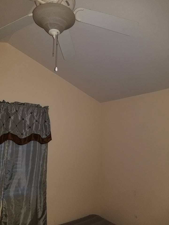 Beige bedroom corner with ceiling fan and curtained window