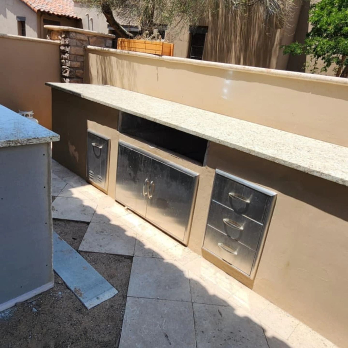 Outdoor built-in stone grill with metal cabinet doors and tan stucco wall in a courtyard