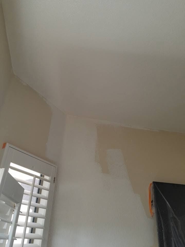 Partially painted beige wall and ceiling in a room with a shuttered window and covered furniture