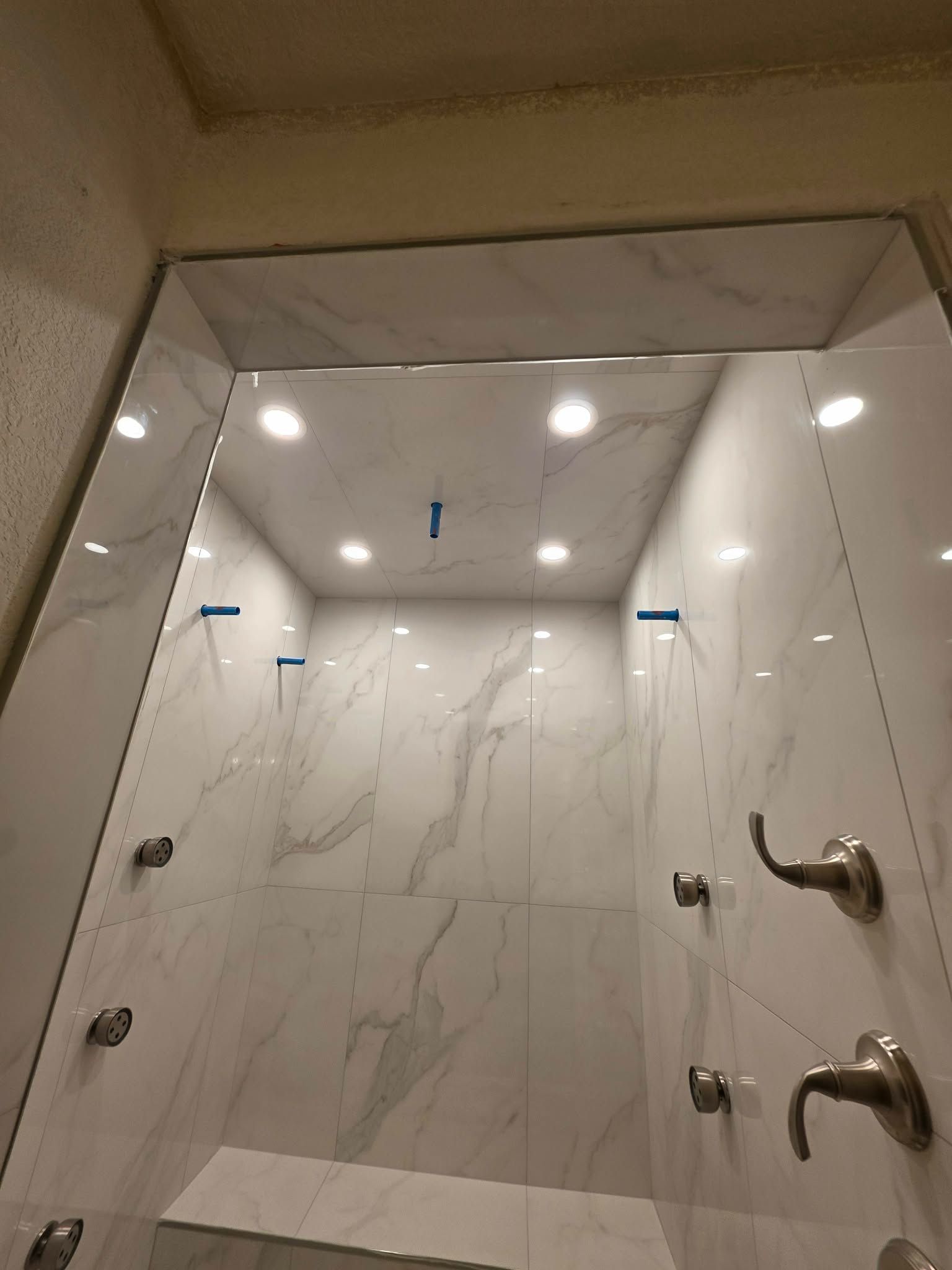 Modern walk-in shower with white marble-look tile, recessed lights, and chrome fixtures