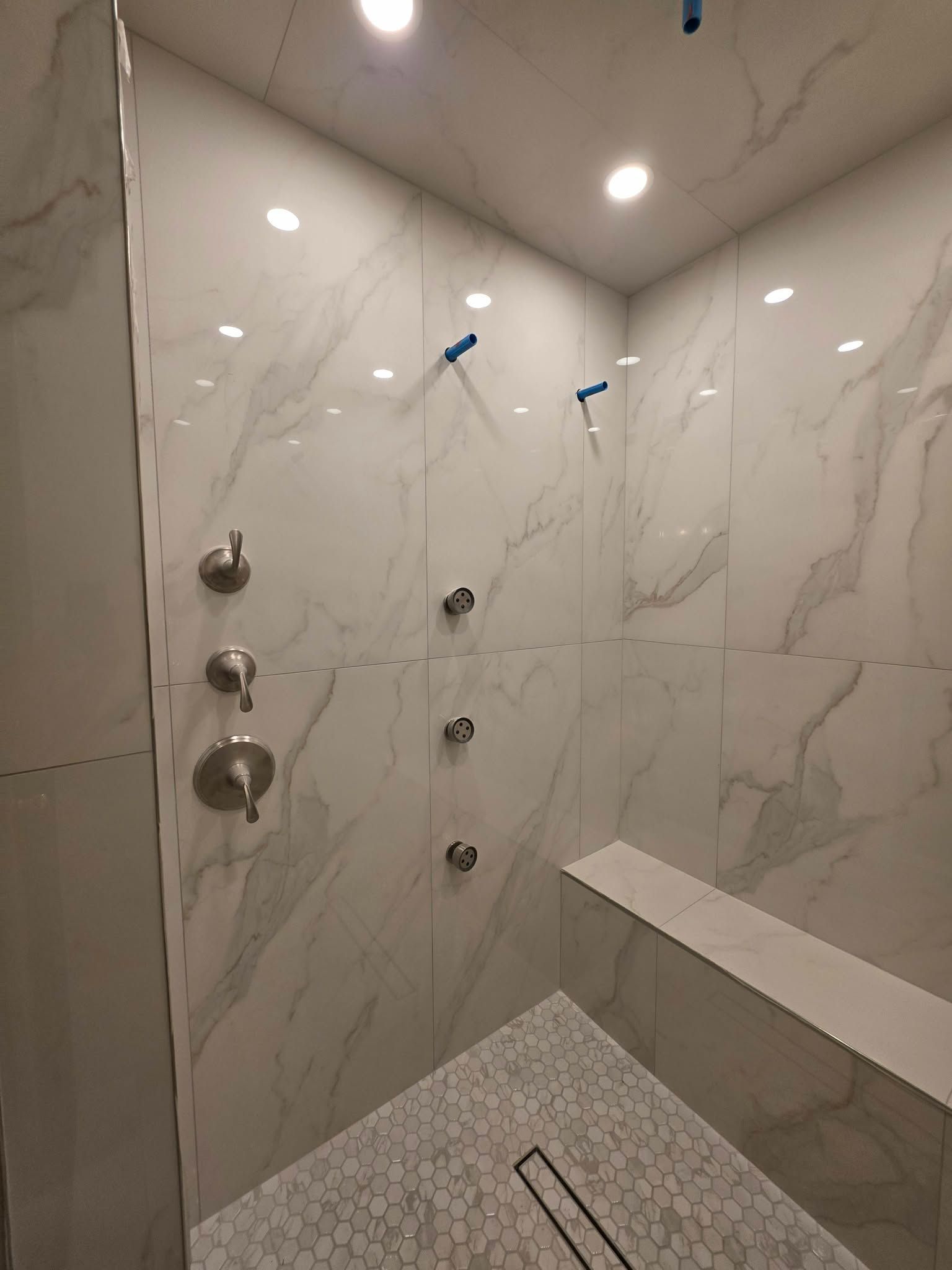 Modern marble-tiled shower with multiple chrome shower controls and a pebble-floored drain area.