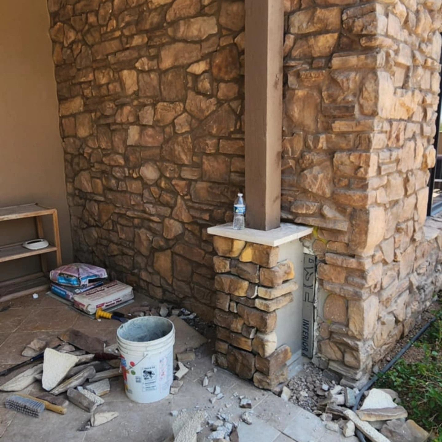 Stone wall under construction with scattered tools, debris, and a bucket in a partially finished room