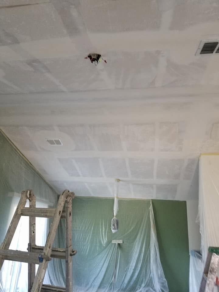 Room under renovation with a ladder, plastic-covered wall, and unfinished ceiling patches