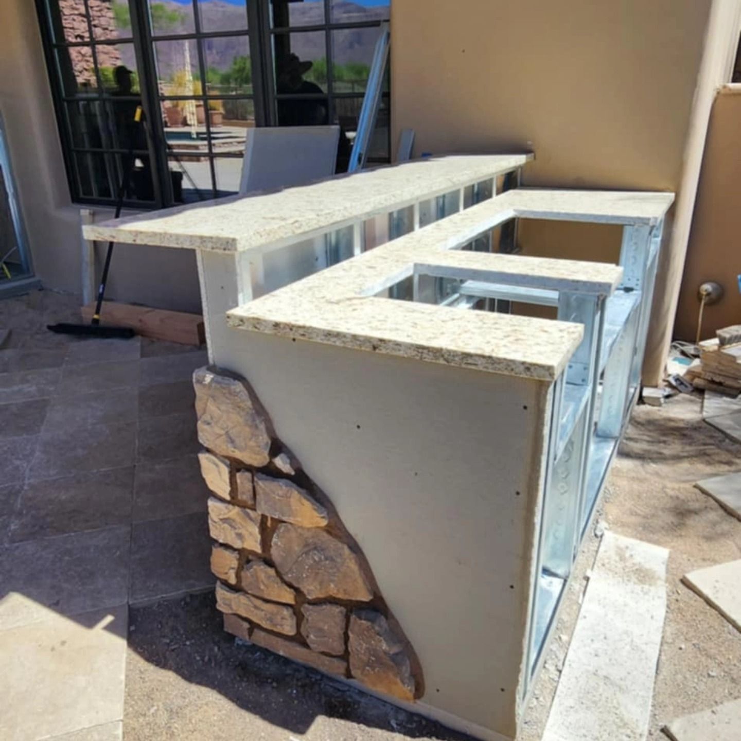 Outdoor stone-and-concrete bar counter under construction beside a windowed patio.