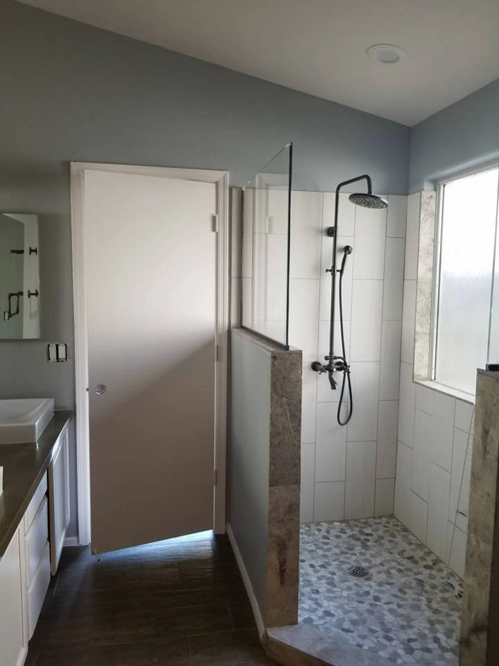 Bathroom with open door, walk-in shower, glass partition, and window light.