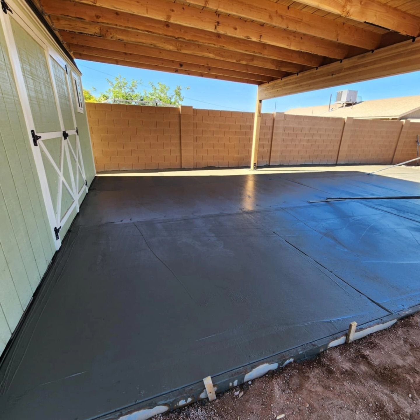 Covered patio with a fresh black epoxy floor and white storage cabinets beside a tan fence