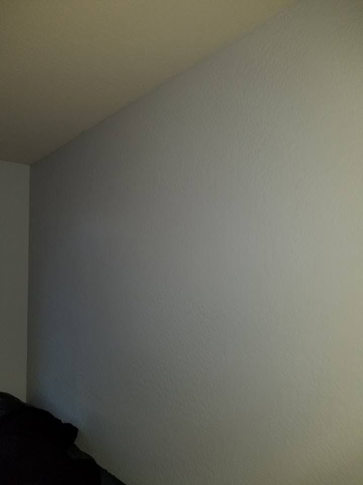 Empty white wall in a dimly lit room with a dark object in the lower left corner