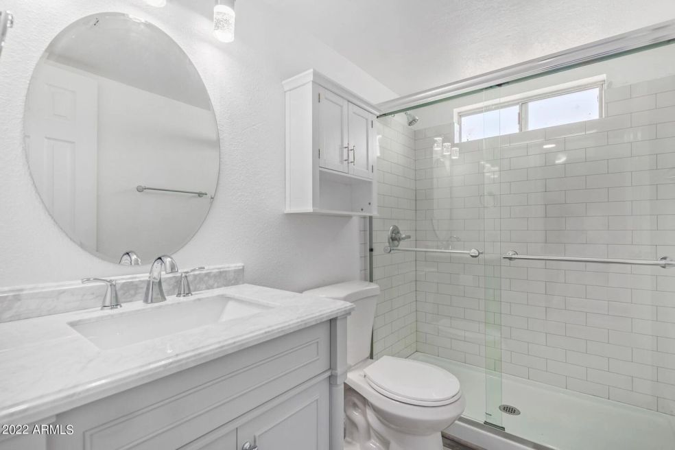Bright white bathroom with vanity, round mirror, and glass-enclosed shower.