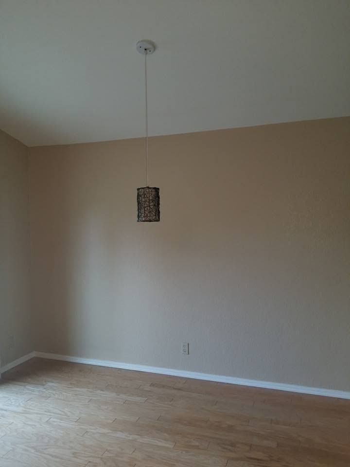 Empty beige room with wood floor and a hanging ceiling light fixture