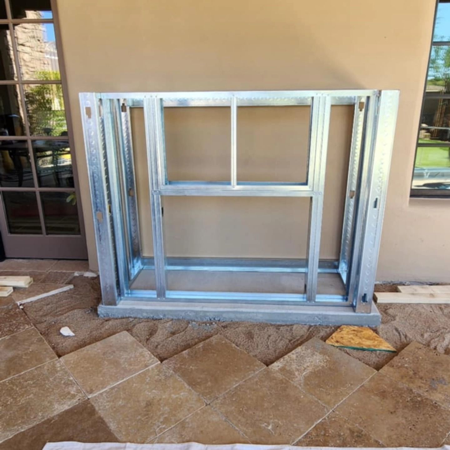 Stacked metal window frames leaning against a beige stucco wall on a tiled patio.