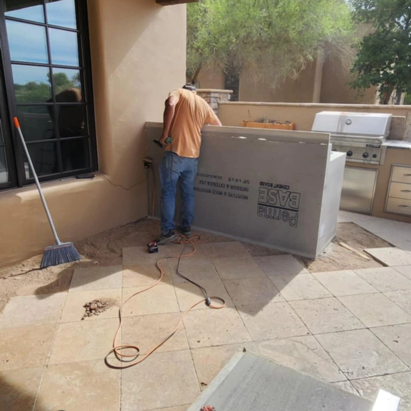 Worker installing a large gray countertop in a tiled outdoor patio kitchen beside a grill