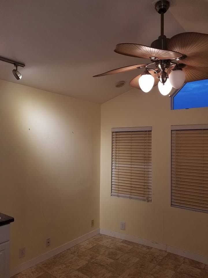Empty beige room with ceiling fan, windows with blinds, and carpeted floor.