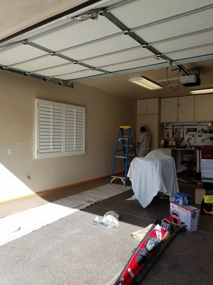 Garage interior with open door, ladder, covered items, and tools on the floor.
