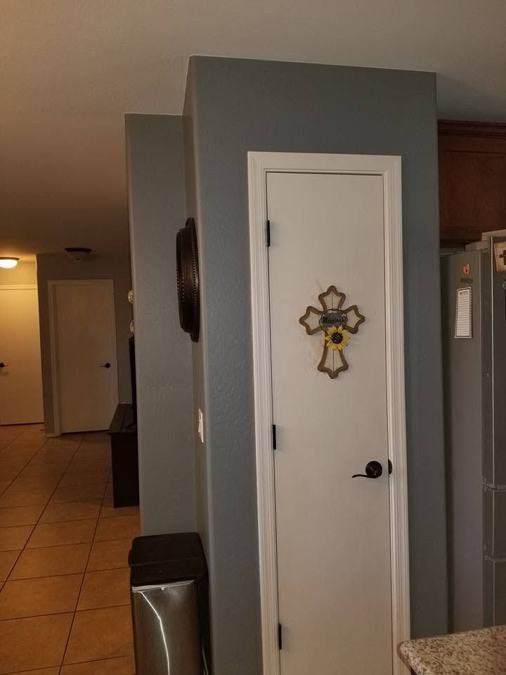 Hallway with a white door featuring a decorative cross, gray walls, and tiled floor