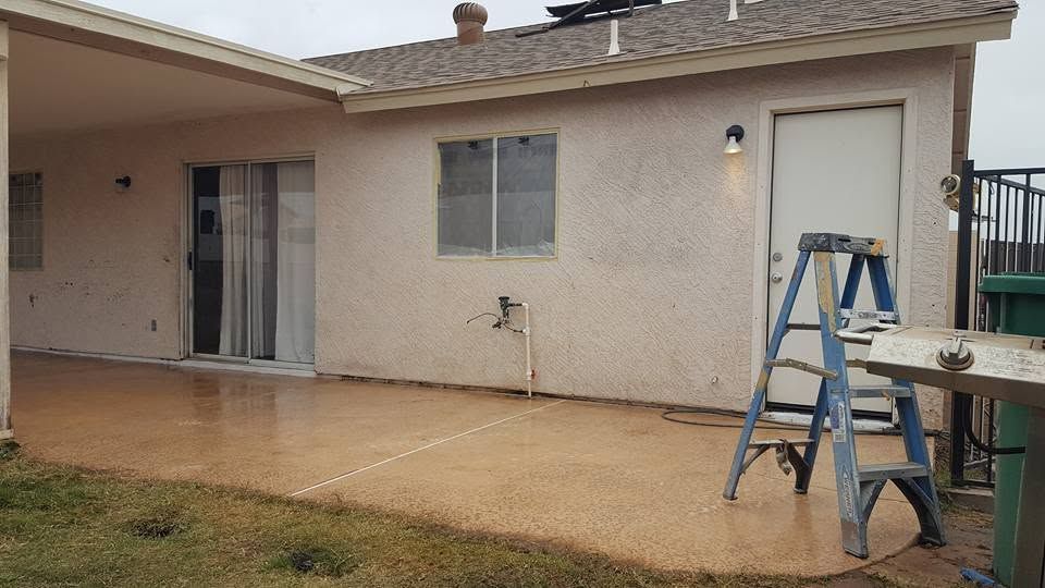 Patio of a beige house with wet concrete, a blue ladder, and outdoor furniture under a cloudy sky
