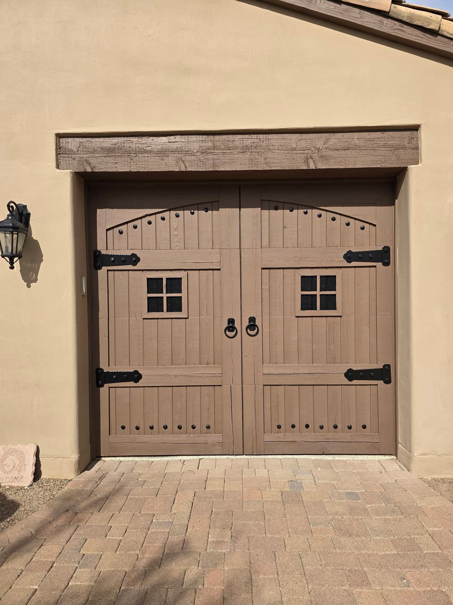 Wooden double garage doors with black hardware and small windows in a beige stucco wall.