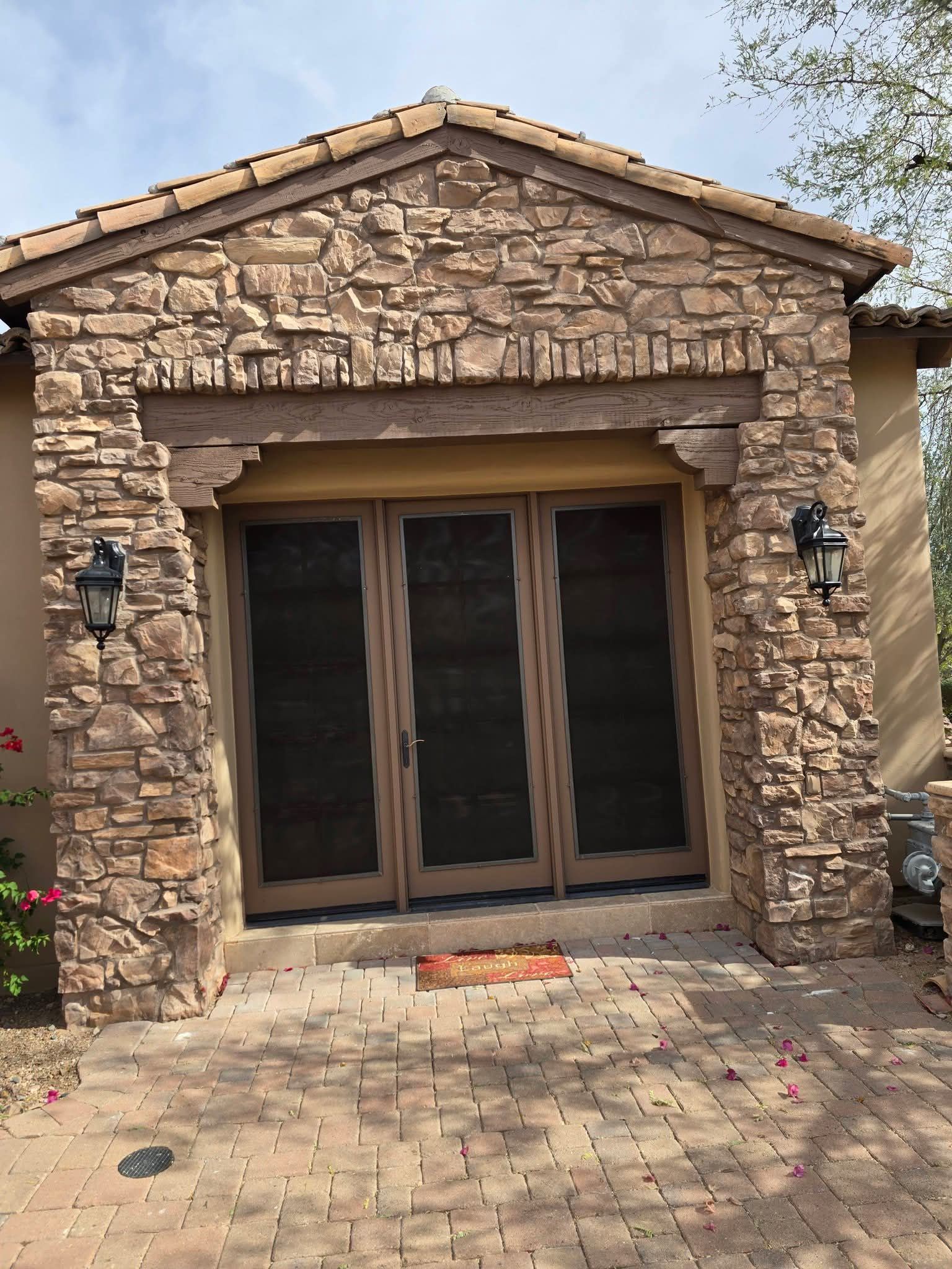 Stone-front home entrance with large dark-framed glass doors and wall lanterns beneath a gabled roof