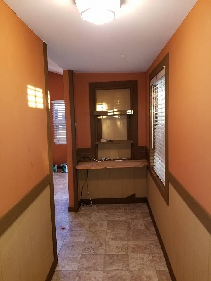Narrow hallway with tan walls, tiled floor, and a small table at the far end beside a mirror.
