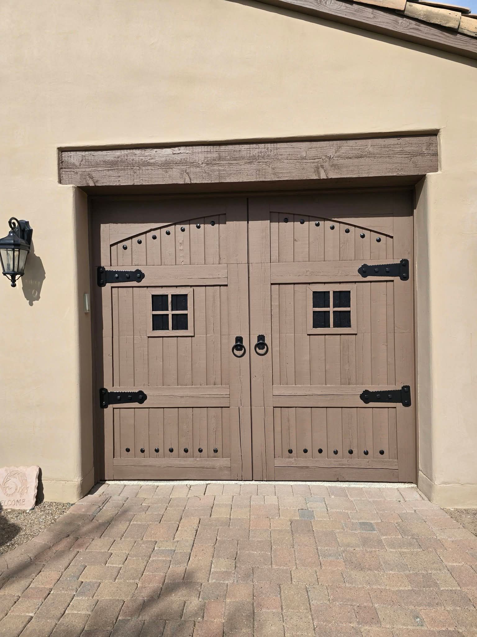 Tan double wooden carriage doors with black hinges on a stucco garage