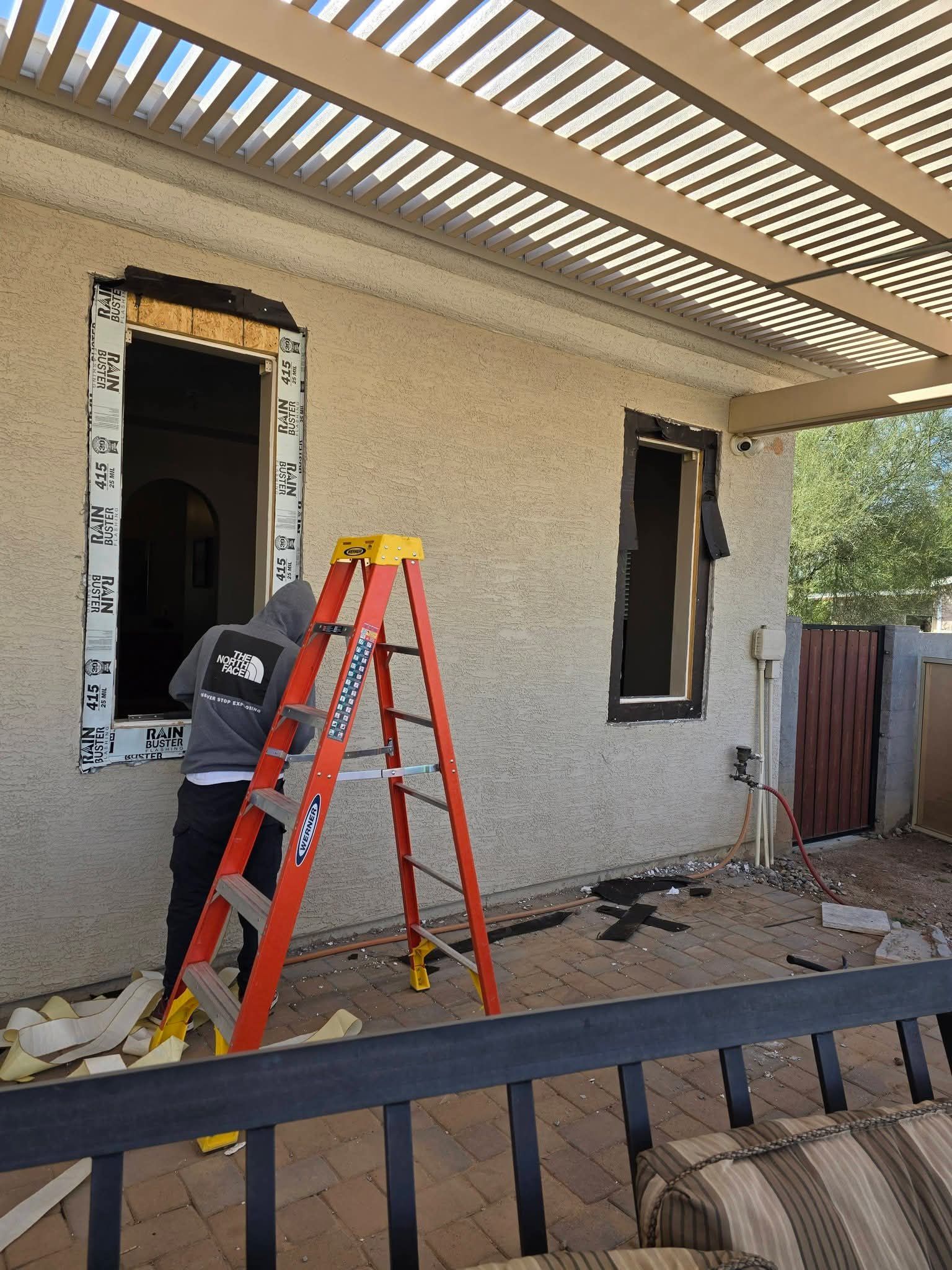 Person on a red ladder working on a house exterior under a patio roof