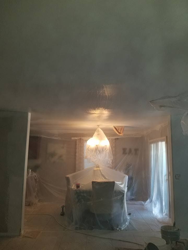 Damaged living room with plastic sheeting, a hanging ceiling light, and cluttered furniture after renovation or fire damage