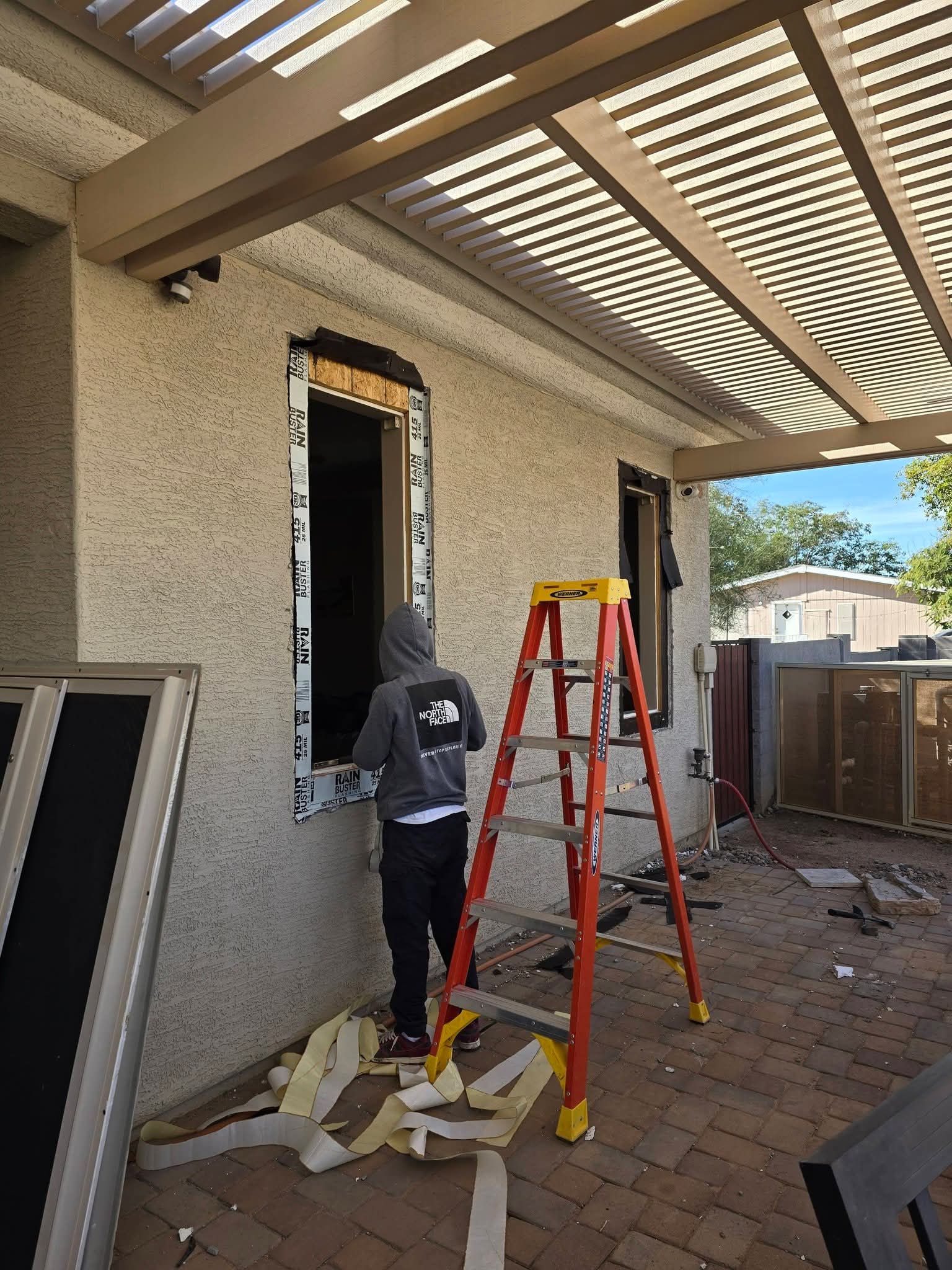 Worker on a ladder installing trim around a doorway under a covered patio.