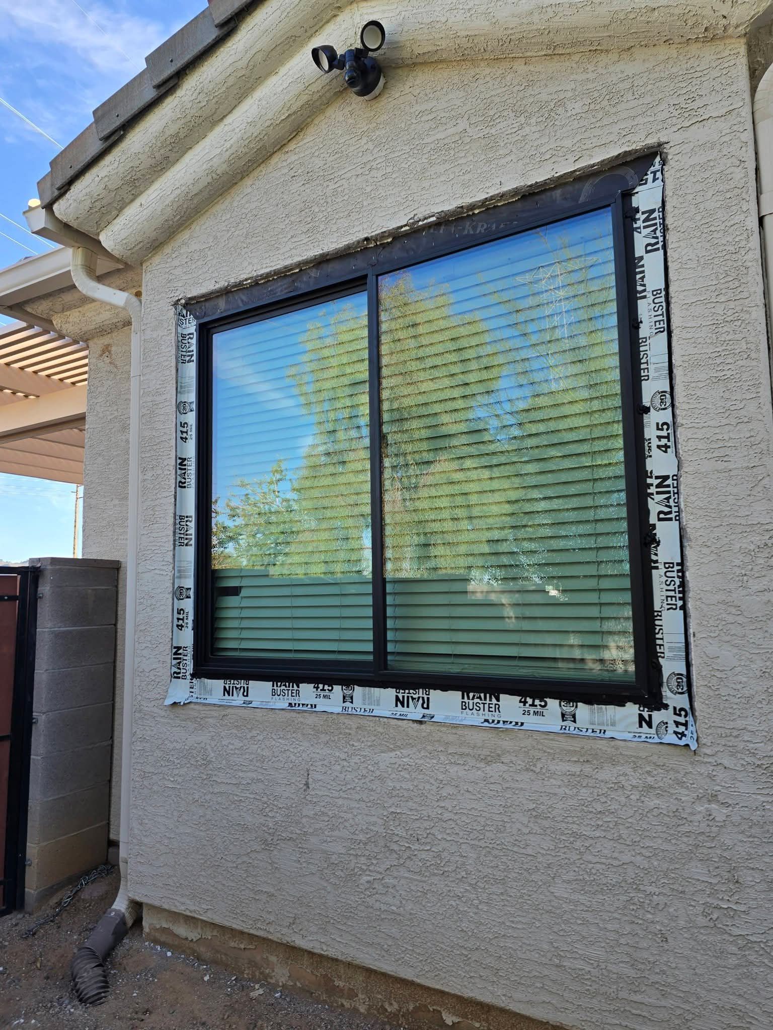 Exterior wall with a double-pane window, stucco siding, and reflection of trees and sky