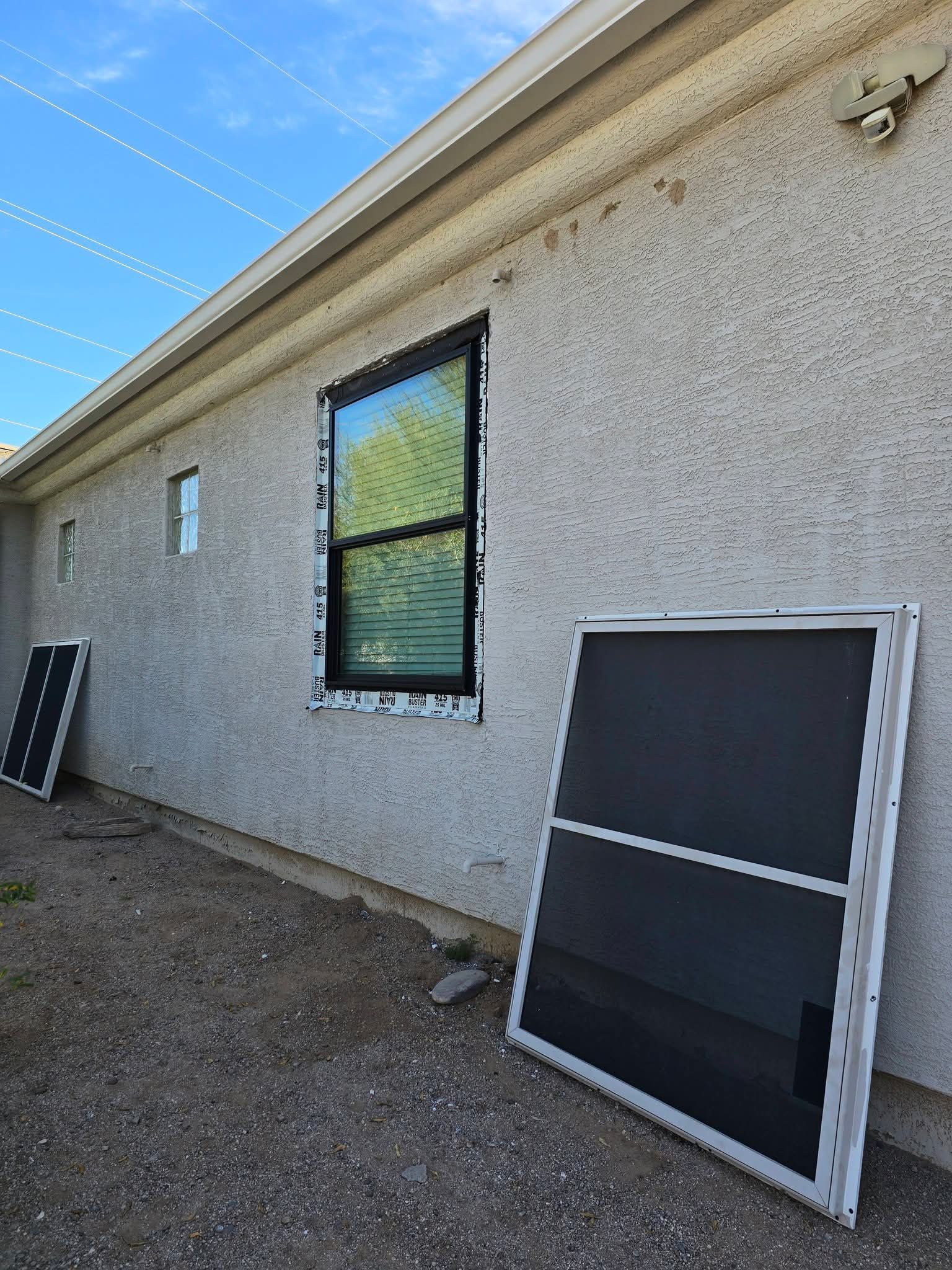 Exterior stucco wall with windows and a detached screen leaning against it in a gravel yard.