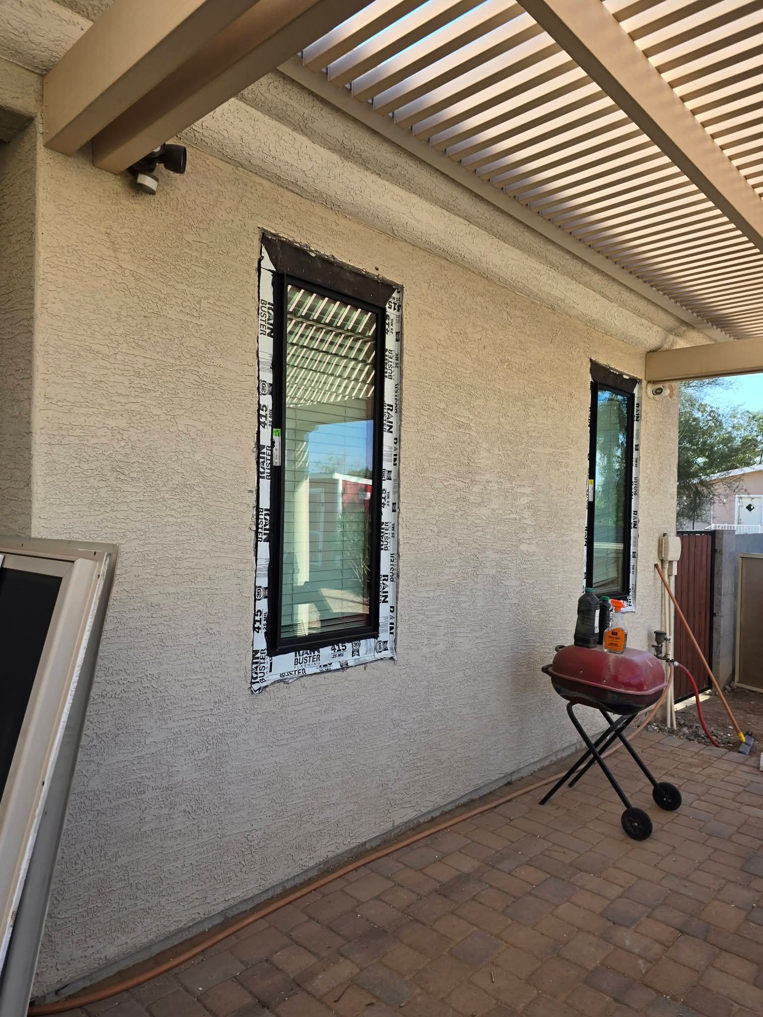 Covered patio with speckled wall, narrow window, brick floor, and a small grill on a stand.