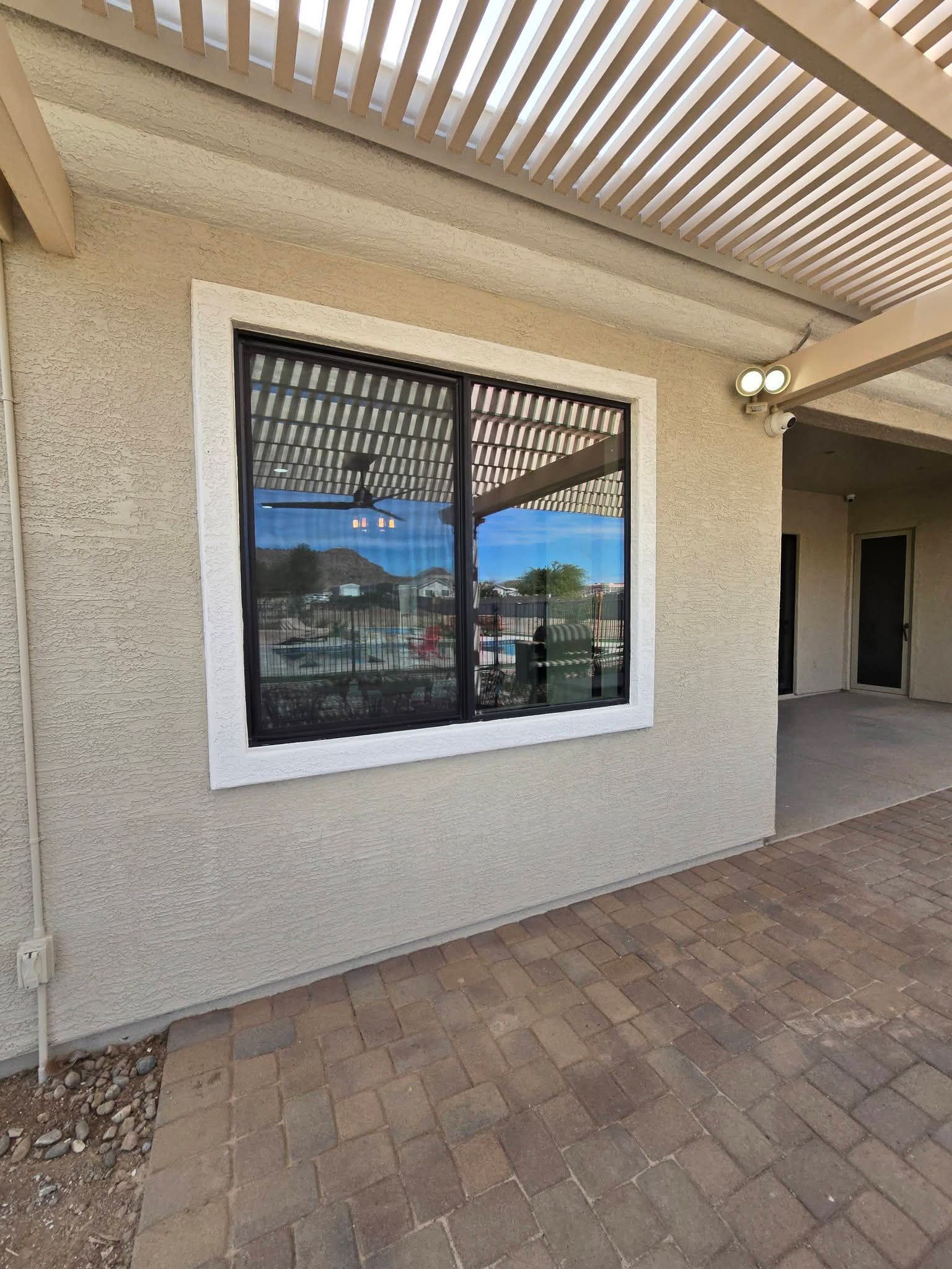 Exterior stucco wall with a white-framed window under a covered walkway, reflecting mountains and sky.