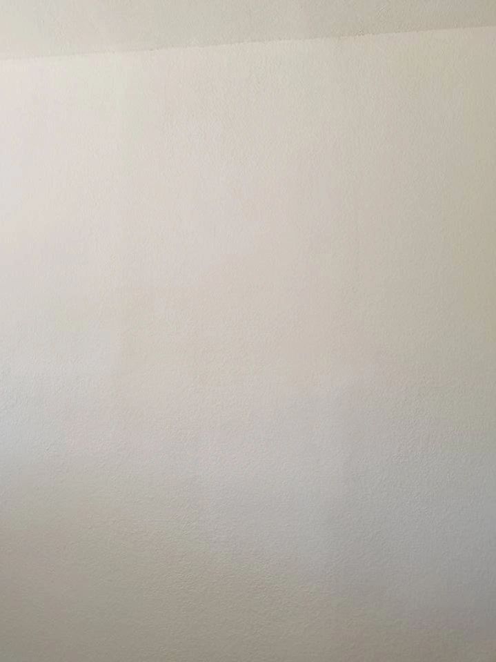 Blank off-white wall with subtle shadows and a slight corner line.