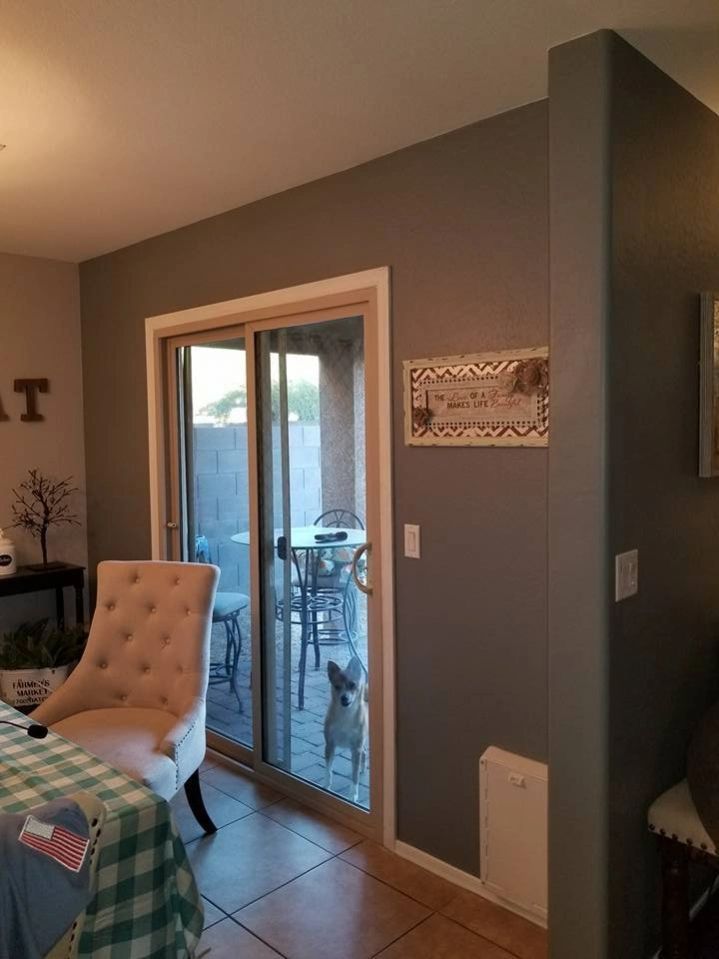 Interior room with sliding glass door to a patio, beige chair, tiled floor, and gray accent wall.