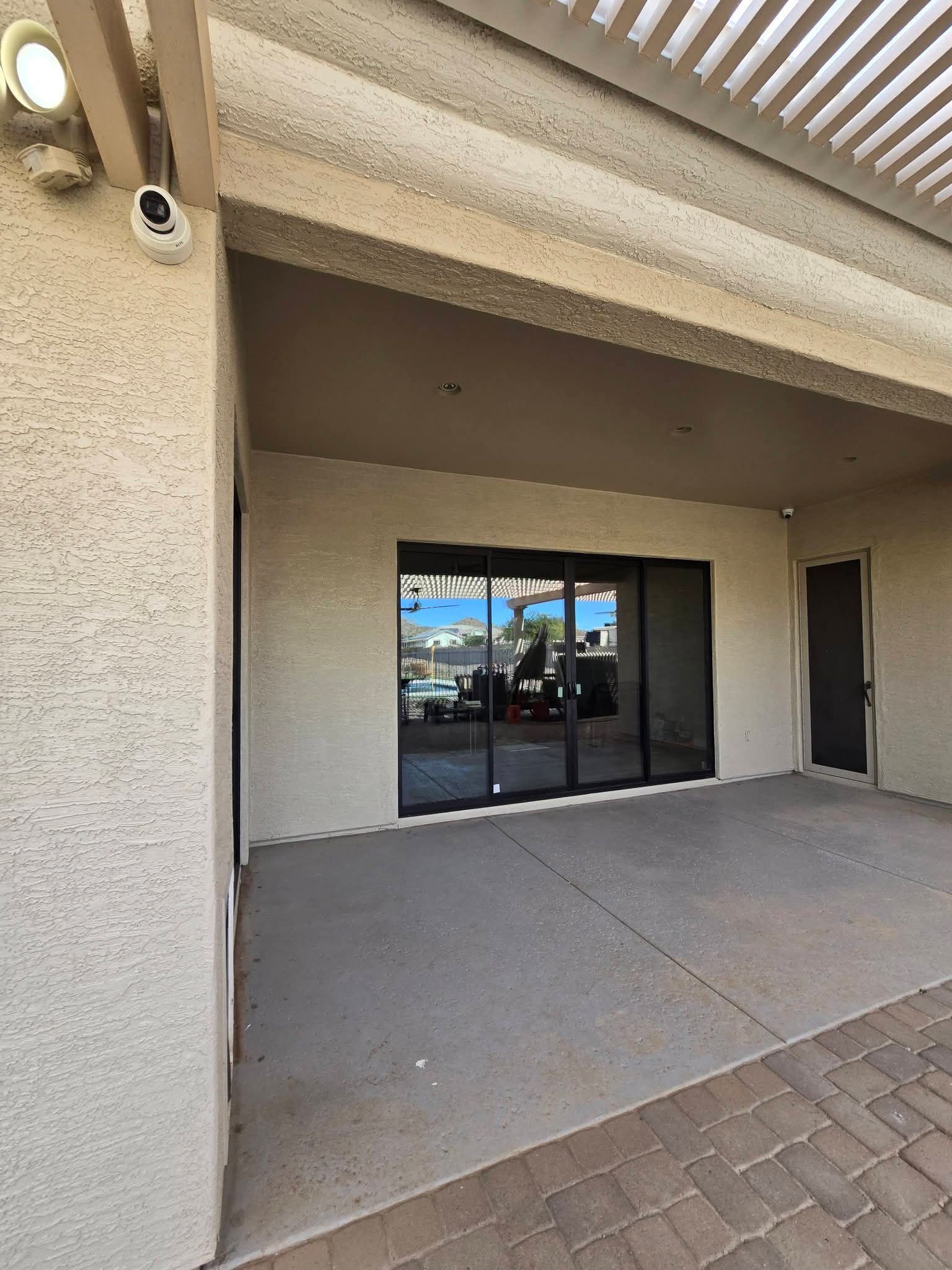 Covered patio with sliding glass doors and a side entry door, viewed from a brick walkway.