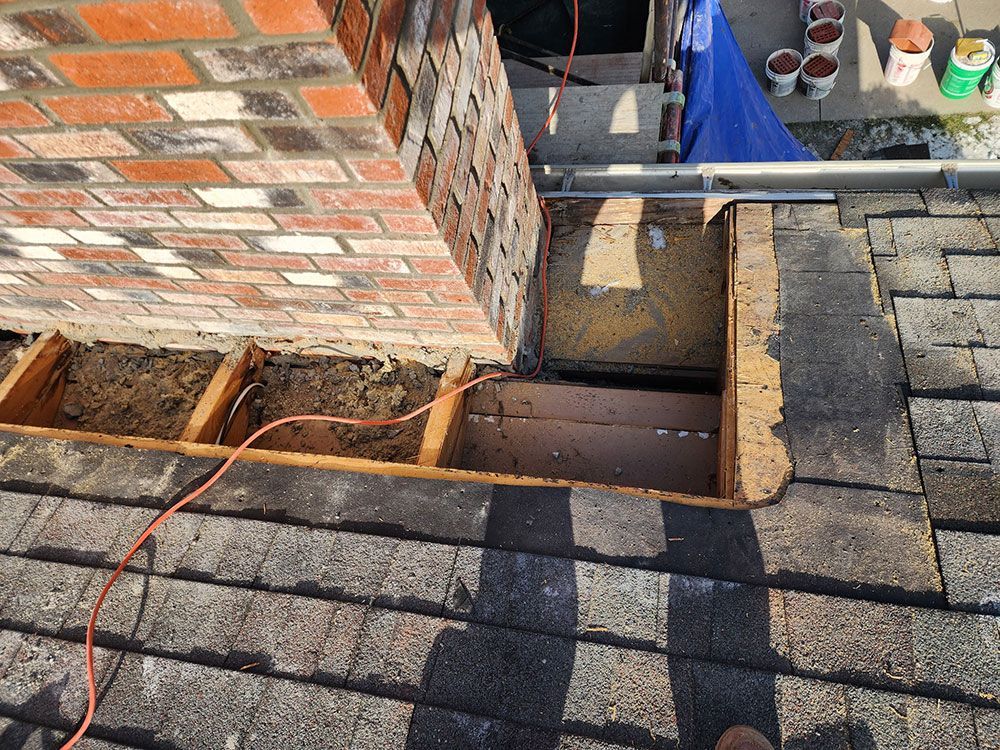 A brick chimney is being removed from the roof of a house.