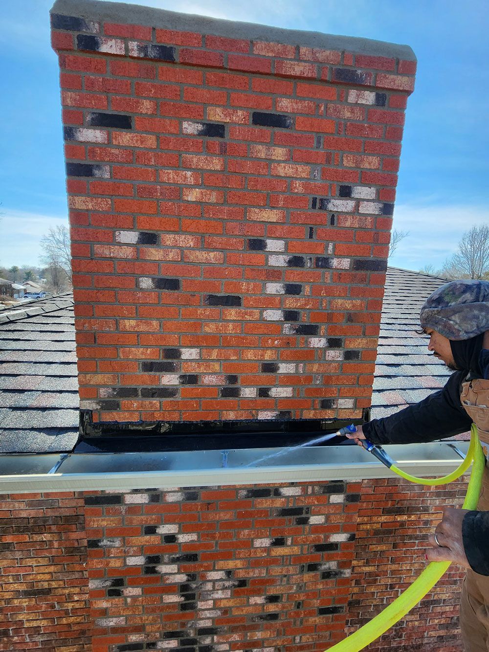A man is spraying a brick chimney with a hose.