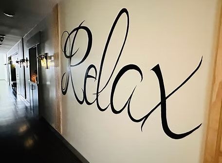 Hallway wall with large black cursive word “Relax” painted on a white surface