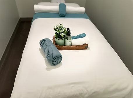 Spa treatment table with rolled blue towels, candles, and a small plant on a white bed