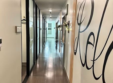 Narrow hallway with glossy floor, wall art, and doors leading to a bright room at the end.
