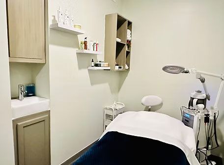 Exam room with a treatment table, medical equipment, cabinets, and shelves on white walls