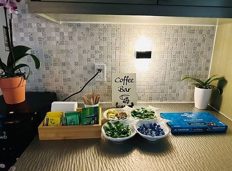 Kitchen counter with coffee station, potted plants, and bowls of fruit and snacks against a mosaic backsplash