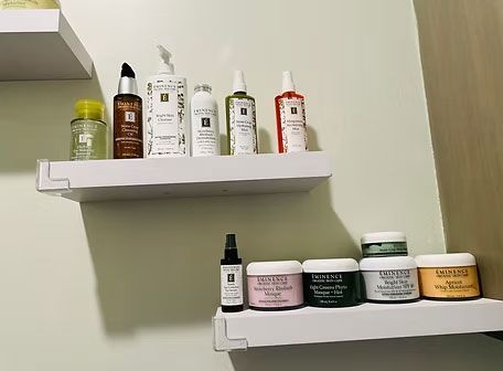 Two wall shelves holding assorted skincare and cosmetic bottles and jars