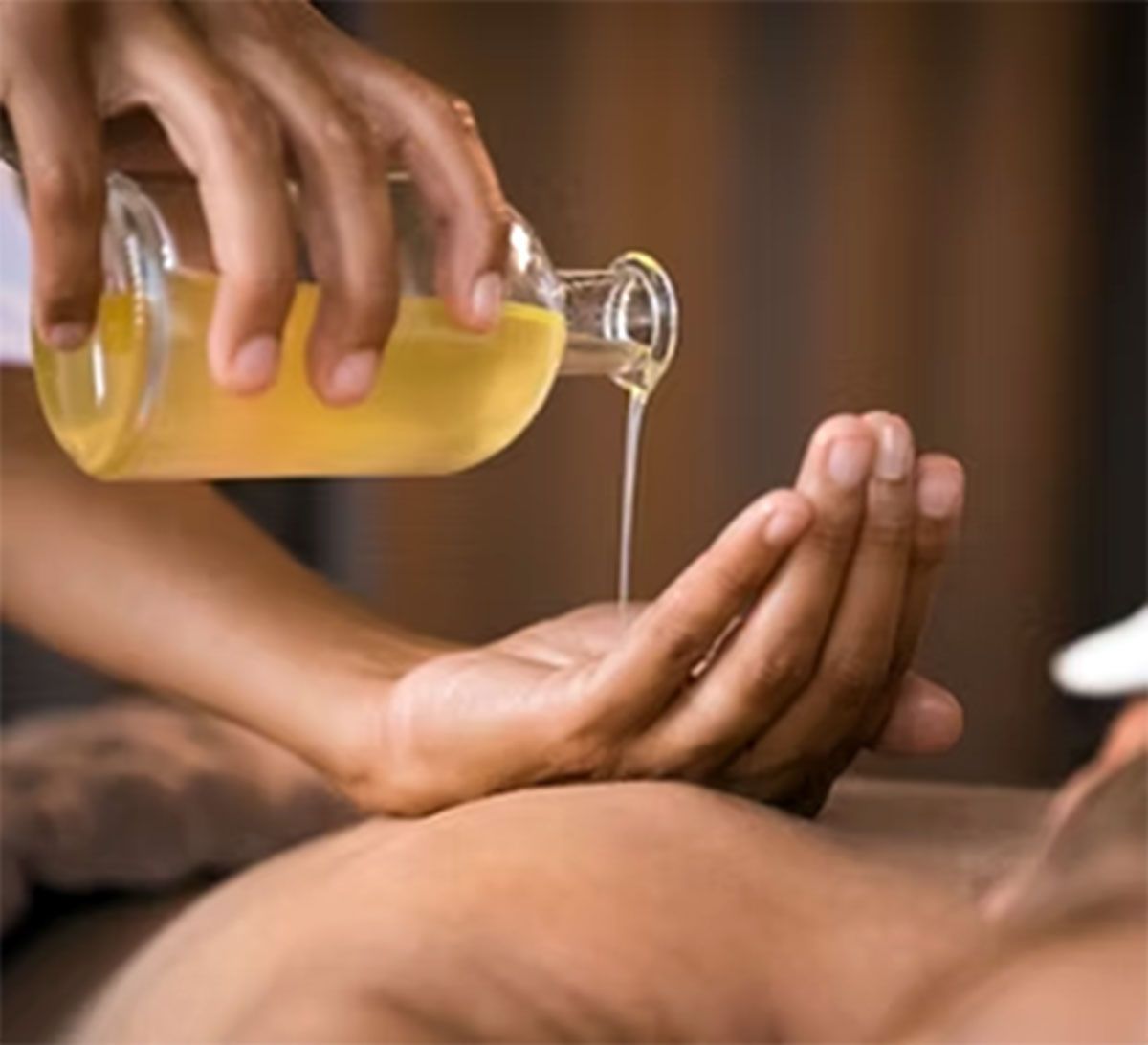 Oiled liquid poured from a bottle onto a person's cupped hands during a massage