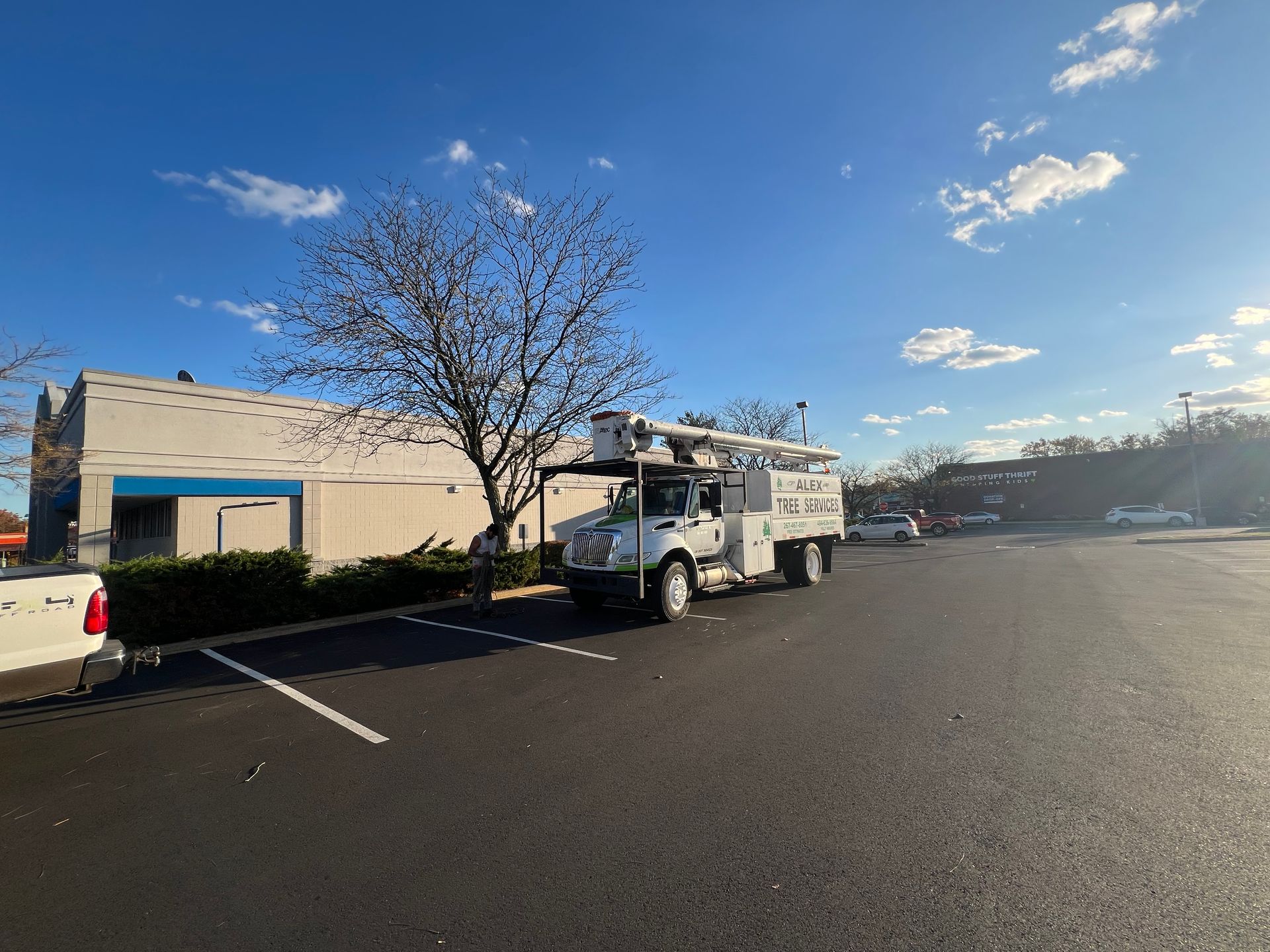 A white utility bucket truck parked in a large asphalt parking lot during the day, with a building in the background.