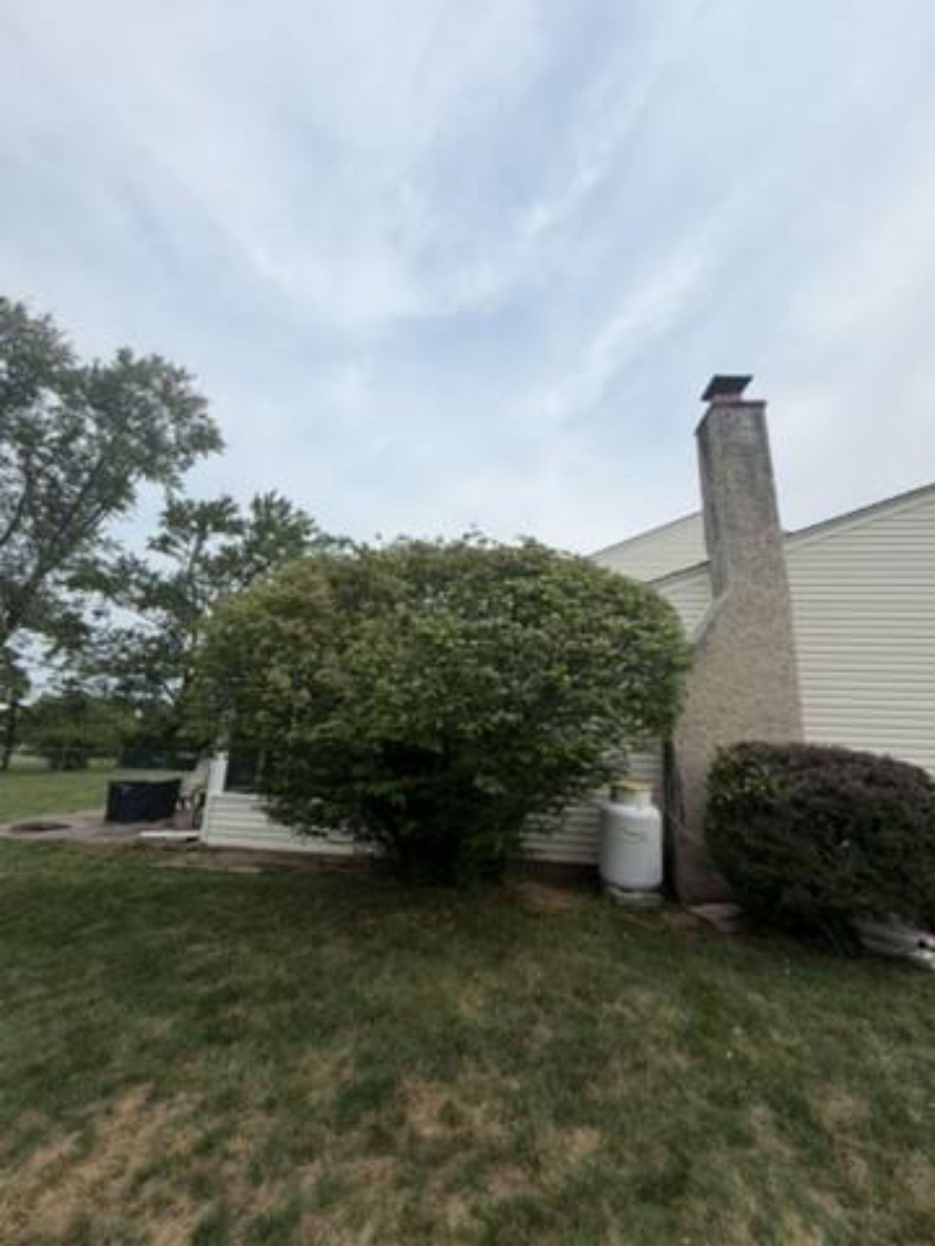 Suburban house exterior with a chimney, bushes, lawn, and cloudy sky.