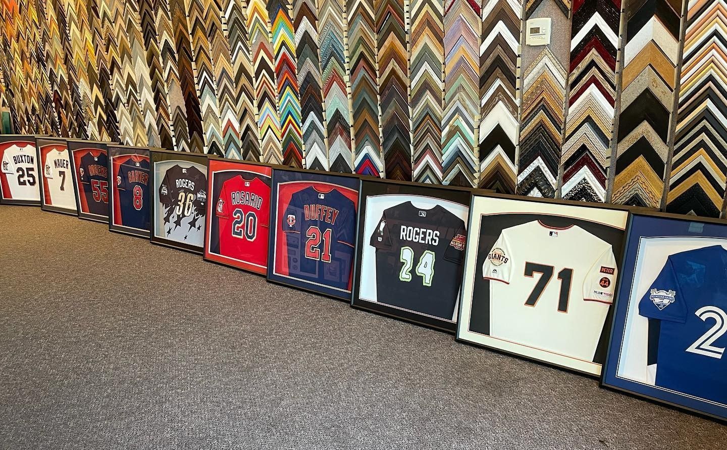 Framed sports jerseys lined up on display; various colors with ornate frame backgrounds.
